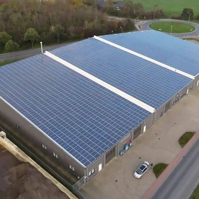 Eine sehr große Gewerbehalle vor einem Kreisverkehr mit vielen Photovoltaikmodulen auf dem Dach.